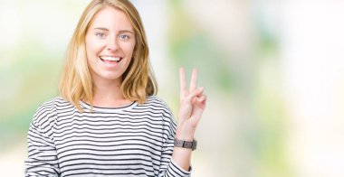 Mutlu yüz zafer işareti yaparken kameraya göz kırpıyor ile gülümseyen izole arka plan üzerinde çizgili süveter giyen güzel genç kadın. İki numaralı.