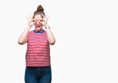 Casual göz dilini, parmaklarının arasından baktığını yapışmasını dürbün gibi ok jest yapıyor izole arka plan üzerinde giyen güzel esmer kıvırcık saçlı Genç kız. Deli ifade.