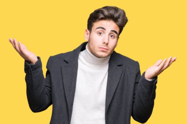 Üzerinde kış ceket giyen genç zarif adam arka plan clueless ve şaşkın bir ifadeyle kollar ve eller kaldırdı izole. Şüphe kavramı.