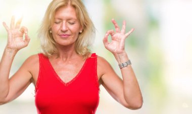 Orta yaş sarışın kadın izole arka plan üzerinde dinlenmek ve gülümseyen gözlerle parmak ile meditasyon jest yapıyor kapalı. Yoga kavramı.