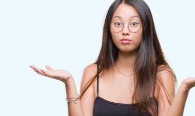 Üzerinde gözlük takan Genç Asyalı kadın arka plan clueless ve şaşkın bir ifadeyle kollar ve eller kaldırdı izole. Şüphe kavramı.