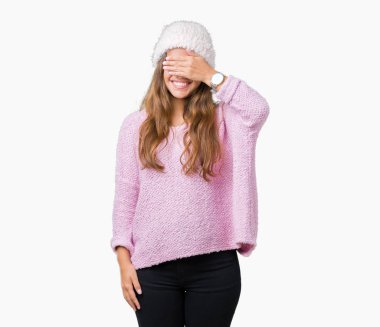 Gülümsüyor ve gözleri için sürpriz kapsayan yüz el ile gülüyor izole arka plan üzerinde kazak ve kış şapka giyen genç güzel esmer kadın. Kör kavramı.