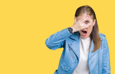 Mahcup ifadeyle parmaklarımın arasından seyir yüz ve gözler el ile kapsayan şok izole arka plan bakmak üzerinde moda deri ceket giymiş güzel orta yaş Olgun kadın.