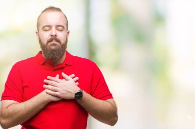 Göğüs kapalı gözlerle ellerinde ve yüzünde minnettar jest ile gülümseyen izole arka plan üzerinde kırmızı gömlek giymiş genç beyaz hipster adam. Sağlık kavramı.