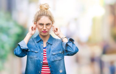 Yüksek sesle müzik gürültü rahatsız ifade parmaklarıyla kulaklarıyla kapsayan izole arka plan üzerinde gözlük takan genç güzel sarışın kadın. Sağır kavramı.