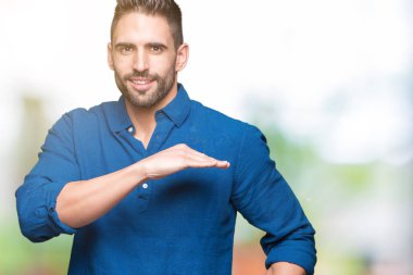 Yakışıklı delikanlı ile büyük ve büyük boy işaret, ölçü birimi sembol gösteren el eller izole arka plan üzerinde. Kameraya bakarak gülümsüyordu. Ölçüm kavramı.