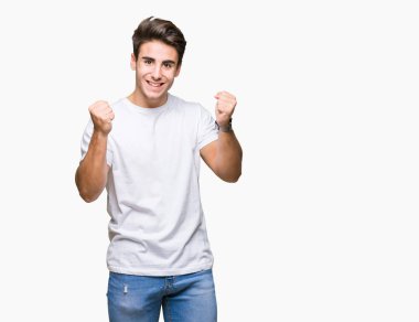 Yakışıklı delikanlı izole arka plan kutlama üzerinde beyaz t-shirt giyen şaşırttı ve silah ile başarı için yükseltilmiş ve açık gözler hayrete düşürdü. Kazanan kavramı.
