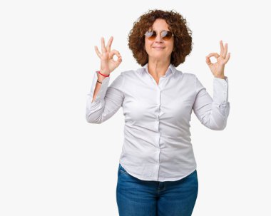 Güzel orta ager üst düzey iş kadın giyiyor güneş gözlüğü izole arka plan üzerinde dinlenmek ve gülümseyen gözlerle kapalı parmak jestle meditasyon yapıyor. Yoga kavramı.