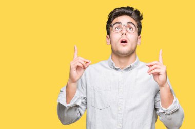 Yakışıklı delikanlı hayrete ve yukarıya bakıyor ve parmakları ile işaret ve silah kaldırdı sürpriz izole arka plan üzerinde gözlük.