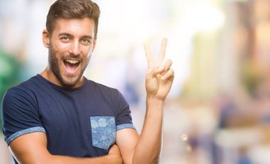 Mutlu yüz zafer işareti yaparken kameraya göz kırpıyor ile gülümseyen izole arka plan üzerinde genç yakışıklı adam. İki numaralı.