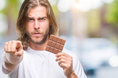 Yakışıklı delikanlı izole arka kamera ve size parmak ile işaret üzerine çikolata yeme uzun saçlı, el işareti, pozitif ve kendinden emin bir jest ön