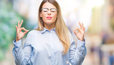Genç güzel iş kadın gözlük izole arka plan üzerinde dinlenmek ve gülümseyen gözlerle kapalı parmak jestle meditasyon yapıyor. Yoga kavramı.
