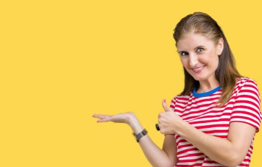Orta yaş Olgun kadın üzerinde rahat t-shirt giyen arka plan gösteren palm el izole ve mutlu ve neşeli gülümseyen thumbs up, ok hareketi ile yapıyor