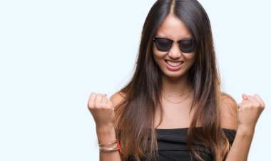 Genç Asyalı kadın üzerinde güneş gözlüğü takıyor arka plan çok mutlu ve heyecanlı kaldırdı, silah ile kazanan jest yapıyor gülümseyen ve başarı için çığlık izole. Kutlama kavramı.