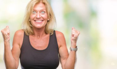 Orta yaş sarışın kadın kutluyor izole arka plan üzerinde şaşırttı ve başarı için kaldırdı kollarını açarak hayret ve gözleri açık. Kazanan kavramı.