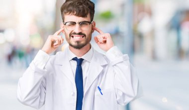 Yüksek sesle müzik gürültü rahatsız ifade parmaklarıyla kulaklarıyla kapsayan izole arka plan üzerinde beyaz önlük giyen genç profesyonel bilim adam. Sağır kavramı.