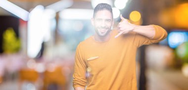 Yakışıklı delikanlı yapıyor gülümseyen izole arka plan üzerinde telefon hareketi ile el ve parmak telefonda konuşuyor gibi. Kavramları iletişim.