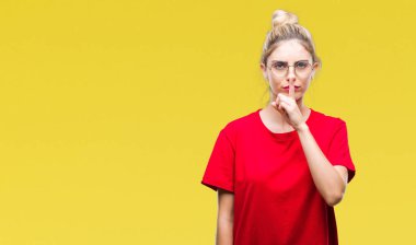 Dudaklarında parmak ile sessiz olmanı izole arka plan üzerinde kırmızı t-shirt ve gözlük giyen genç güzel sarışın kadın. Sessizlik ve gizli kavramı.