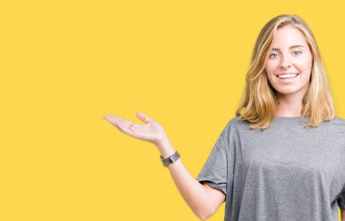 Neşeli sunulması ve kameraya bakarak avucunun ile işaret gülümseyen izole arka plan üzerinde büyük boy rahat t-shirt giyen güzel genç kadın.