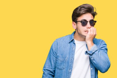 Genç yakışıklı adam stresli ve gergin ile izole arka plan üzerinde güneş gözlüğü takıyor tırnak ısırma dudaklarından eller. Anksiyete sorunu.