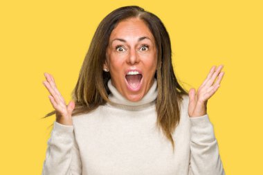 Üzerinde kış kazak giyen güzel orta yaş yetişkin kadın deli kutluyor arka plan izole ve başarı için kaldırdı kollarını açarak hayrete ve heyecanlı çığlık gözleri açık. Kazanan kavramı