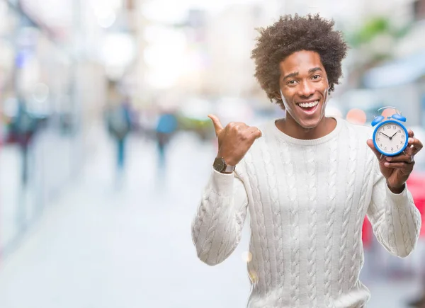 Afro american man holding vintage alarm clock over isolated background pointing and showing with thumb up to the side with happy face smiling