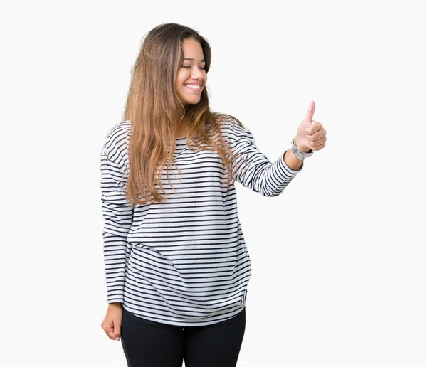 年轻美丽的黑发女人穿着条纹毛衣在孤立的背景看骄傲 微笑做大拇指做手势的身边 — 图库照片