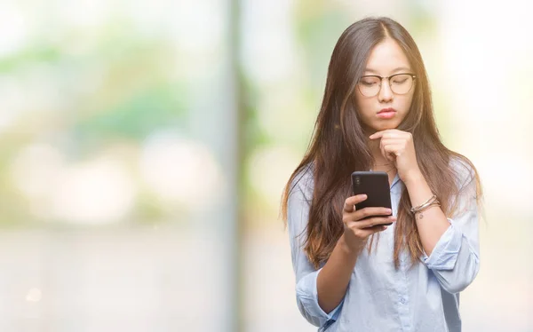 年轻的亚洲妇女发短信使用智能手机在孤立的背景下严肃的面孔思考问题 非常困惑的想法 — 图库照片
