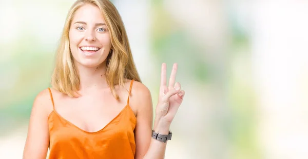 美しい若い女性の勝利のサインを行うカメラでウィンクしている幸せそうな顔を浮かべて孤立の背景にオレンジ色のシャツを着てします — ストック写真