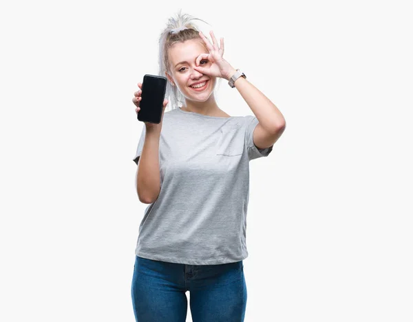 指の間から見て目に手で サインをして笑っている幸せそうな顔で孤立した背景にスマート フォンの若いブロンドの女性表示画面 — ストック写真