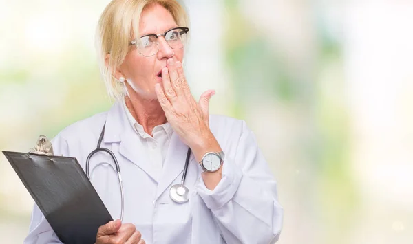 Middle age blonde doctor woman holding clipboard over isolated background cover mouth with hand shocked with shame for mistake, expression of fear, scared in silence, secret concept