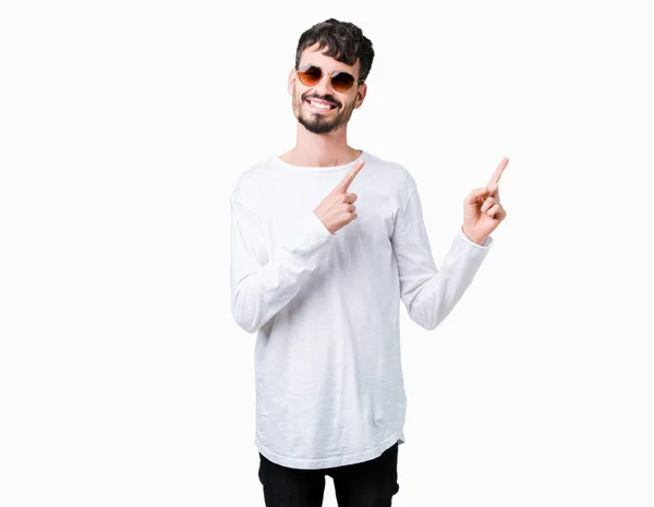 笑顔で側に つの手と指で指しているカメラを見て孤立の背景の上にサングラスをかけている若いハンサムな男 — ストック写真