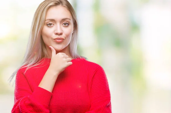 Young blonde woman wearing winter sweater over isolated background looking confident at the camera with smile with crossed arms and hand raised on chin. Thinking positive.