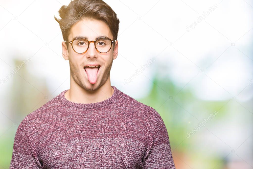 Young handsome man wearing glasses over isolated background sticking tongue out happy with funny expression. Emotion concept.