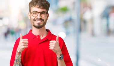 Yakışıklı delikanlı izole arka plan başarı işareti el ile pozitif jest yapıyor üzerinde gözlük takan başparmak gülümseyen ve mutlu. Neşeli bir ifadeyle, kazanan jest kameraya bakıyor.