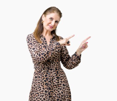 Gülümseyen ve iki elleri ve parmakları ile tarafına işaret kamera bakarak izole arka plan üzerinde leopar elbise giyen güzel orta yaş olgun zengin kadın.