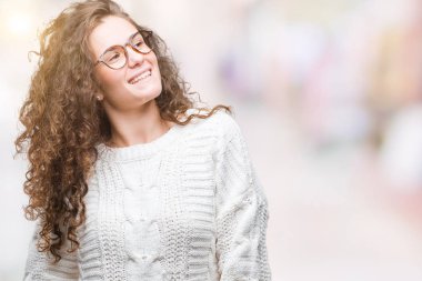 Güzel esmer kıvırcık saçlı Genç kız uzak tarafına yüzünde, doğal ifade gülümseme ile seyir izole arka plan üzerinde kış kazak giyiyor. Kendine güvenen gülüyor.