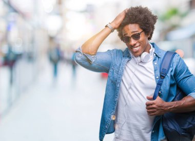 Afro Amerikalı adam giyen kulaklık ve sırt çantası el başında, utanç ve sürpriz ile şok ile vurguladı izole arka plan üzerinde yüz, öfkeli ve sinirli. Korku ve hata için üzgün.