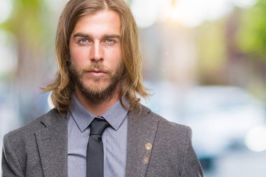 Yüzünde ciddi bir ifade ile izole arka plan üzerinde uzun saçlı Genç yakışıklı iş adamı. Basit ve doğal kameraya bakıyor.