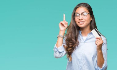 Genç Arap kadın holding kredi izole arka bir fikirle sürpriz üzerinden kartı veya gülen yüz, bir numara ile işaret parmağı soru