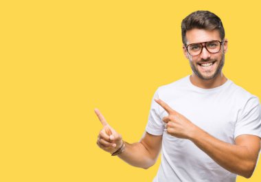 Gülümseyen ve iki elleri ve parmakları ile tarafına işaret kamera bakarak izole arka plan üzerinde gözlük takan genç yakışıklı adam.