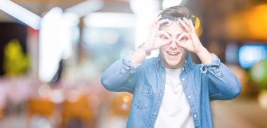 Genç yakışıklı adam, dilini parmaklarının arasından baktığını yapışmasını dürbün gibi ok jest yapıyor izole arka plan üzerinde güneş gözlüğü takıyor. Deli ifade.