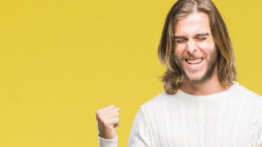 Gülümseyen ve başarı için çığlık genç yakışıklı adam uzun saçlı izole arka plan çok mutlu ve heyecanlı kaldırdı, silah ile kazanan jest yapıyor üzerinde kış kazak giyiyor. Kutlama kavramı.