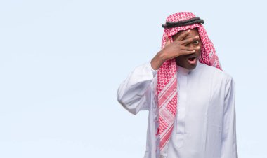 Mahcup ifadeyle parmaklarımın arasından seyir geleneksel keffiyeh yüz ve gözler el ile kapsayan şok bakmak izole arka plan üzerinde giyen genç Arapça Afrika adam.