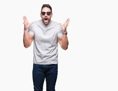 Yakışıklı delikanlı büyük gülümseme ile çığlık zaferini kutluyor ve ellerini kaldırdı izole arka plan çok mutlu ve heyecanlı, kazanan ifade üzerinde güneş gözlüğü takıyor