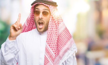 Başarılı fikirle izole arka plan işaret parmağı üzerinde keffiyeh giyen genç yakışıklı adam. Çıktıktan ve mutlu. Bir numara.
