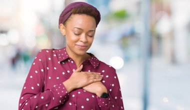 Başörtüsü ile gülümseyen izole arka plan üzerinde giyen güzel genç Afro-Amerikan kadın kapalı gözler ve yüzünde minnettar jest ile göğüs üzerinde eller. Sağlık kavramı.