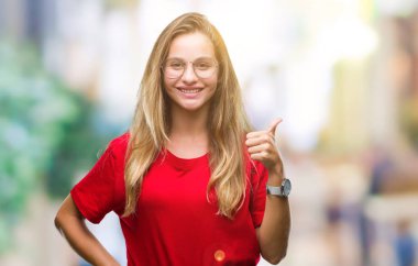 Hareketi el ile mutlu yaşasın yapıyor izole arka plan üzerinde gözlük takan genç güzel sarışın bir kadın. Kameraya bakarak başarı gösteren ile ifade onaylama.