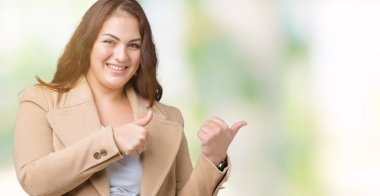 Artı boyutu genç kadın güzel üzerinde kış palto giyiyor izole arka plan emin gülümseyen arkasından el ve kadar başparmak ile işaret