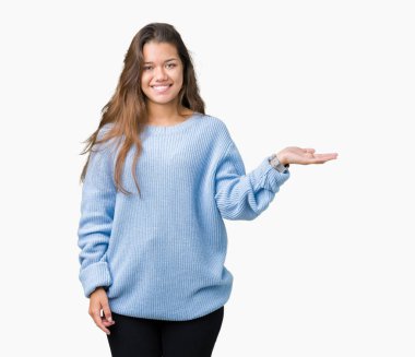 Neşeli sunulması ve kameraya bakarak avucunun ile işaret gülümseyen izole arka plan üzerinde mavi kış kazak giyen genç güzel esmer kadın.